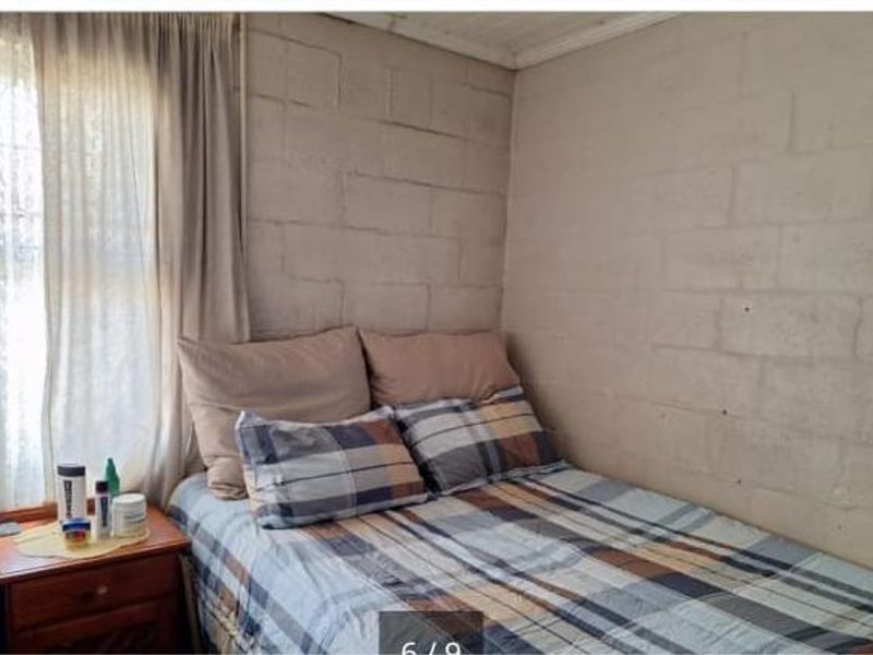 A compact bedroom featuring exposed concrete block walls and a single window with curtains.