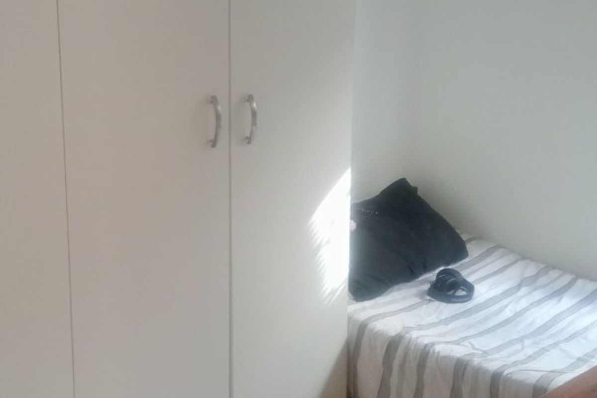 A compact bedroom featuring built-in cupboards and tiled flooring, offering a functional space with neutral finishes.