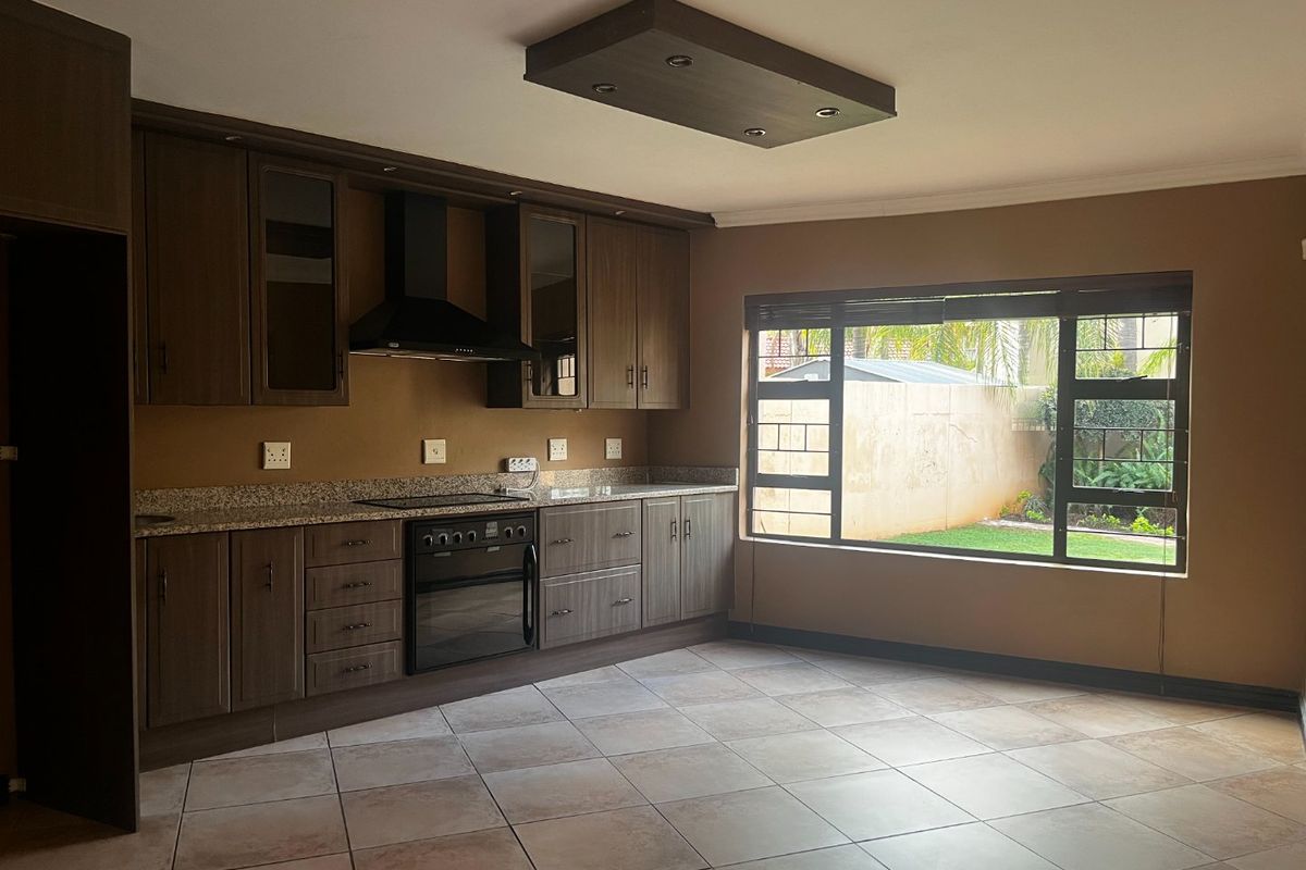 A spacious kitchen featuring dark wood cabinetry, granite countertops, built-in oven and hob, and large windows overlooking the garden.