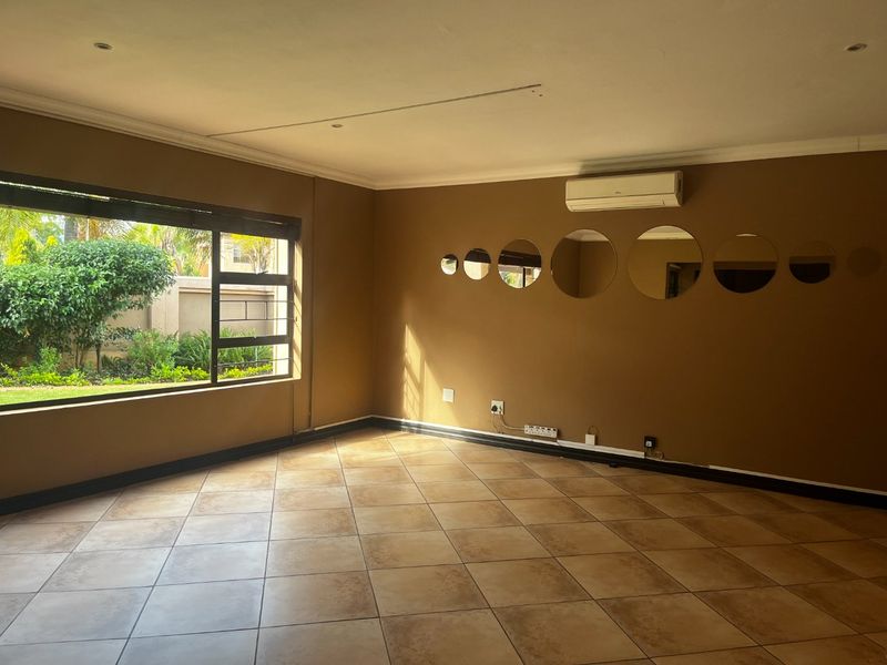 A spacious, empty living room featuring tiled flooring, a wall-mounted air conditioning unit, and large windows overlooking the garden.
