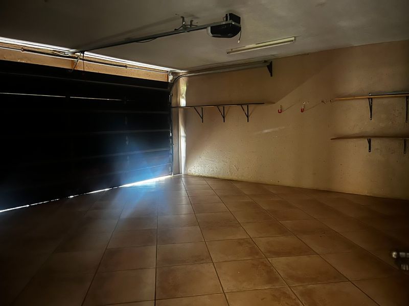 A spacious, empty garage featuring tiled flooring, an automated door mechanism, and wall-mounted storage shelving.