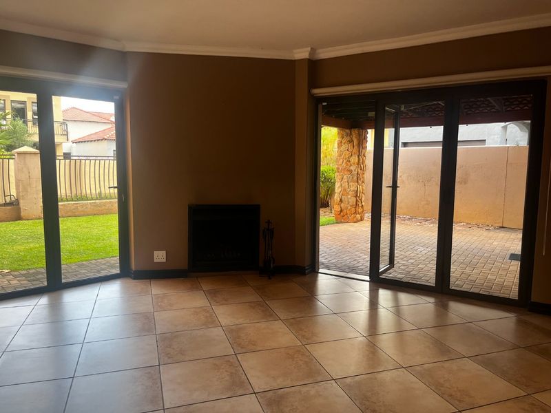 Spacious living room featuring tiled flooring, a built-in fireplace, and large aluminium sliding doors providing direct access to the garden and patio area.