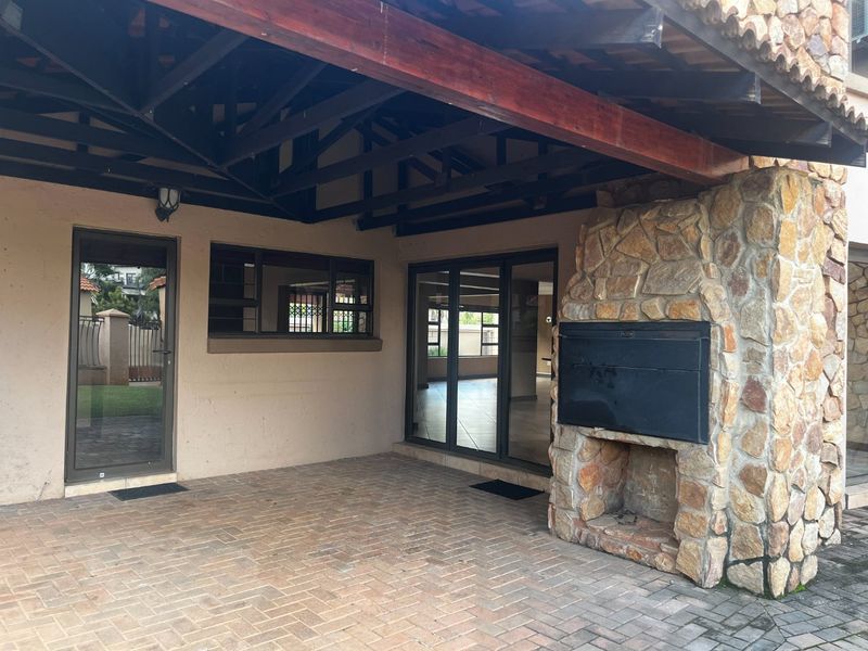 Covered outdoor patio featuring a stone-clad built-in braai, exposed timber beams, and paved flooring, providing a functional space for outdoor entertaining.
