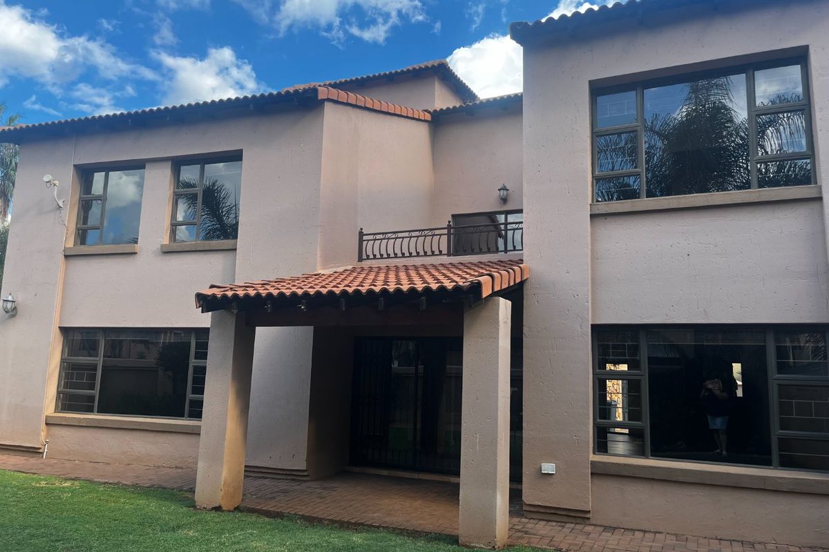 Rear elevation of a two-story house featuring a covered patio, balcony with wrought iron railing, and terracotta roof tiles.