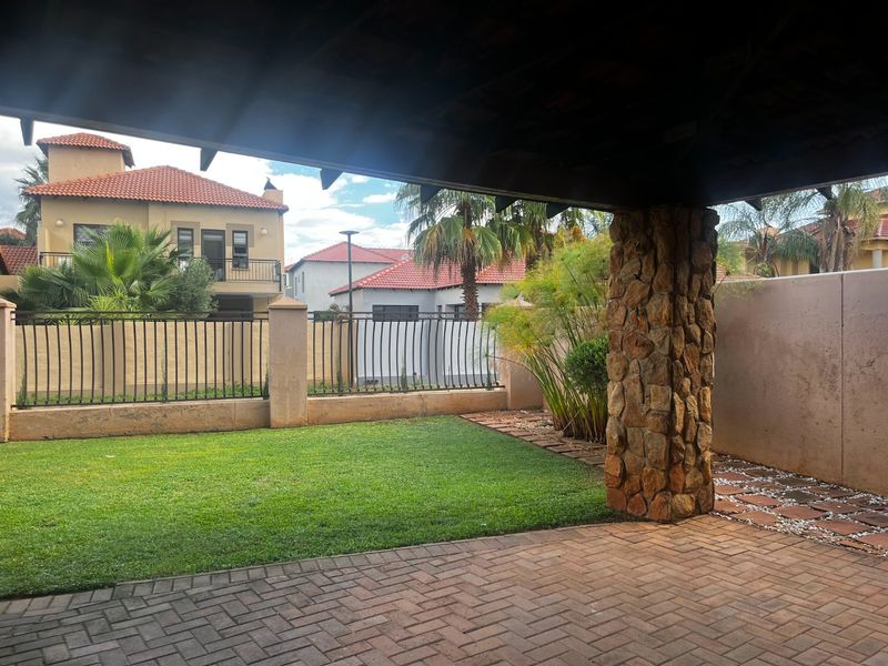 A covered patio area featuring a stone-clad pillar, brick paving, and views over a private garden with secure perimeter fencing.