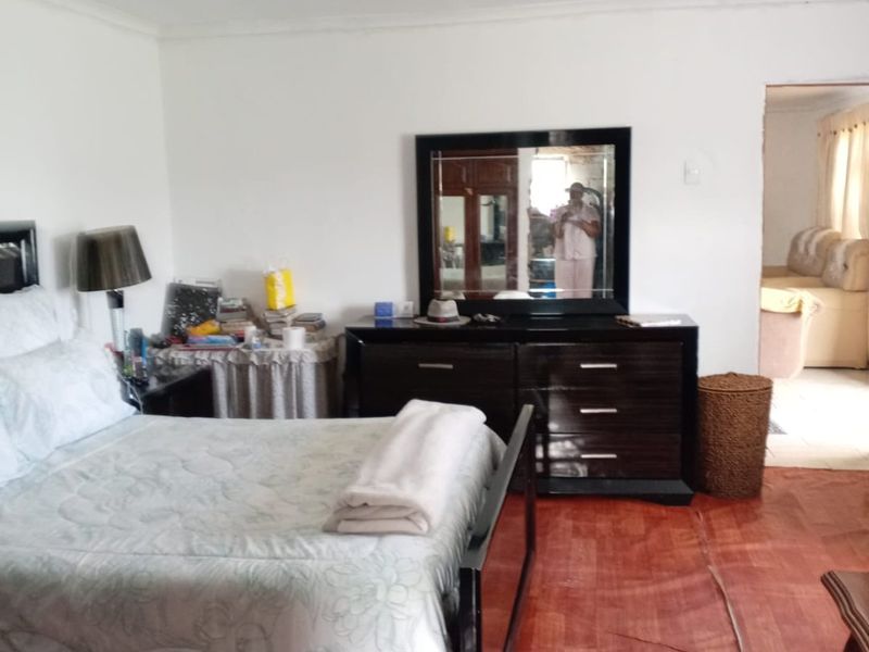 A bedroom featuring laminate flooring and white walls, with a view into an adjacent living space.
