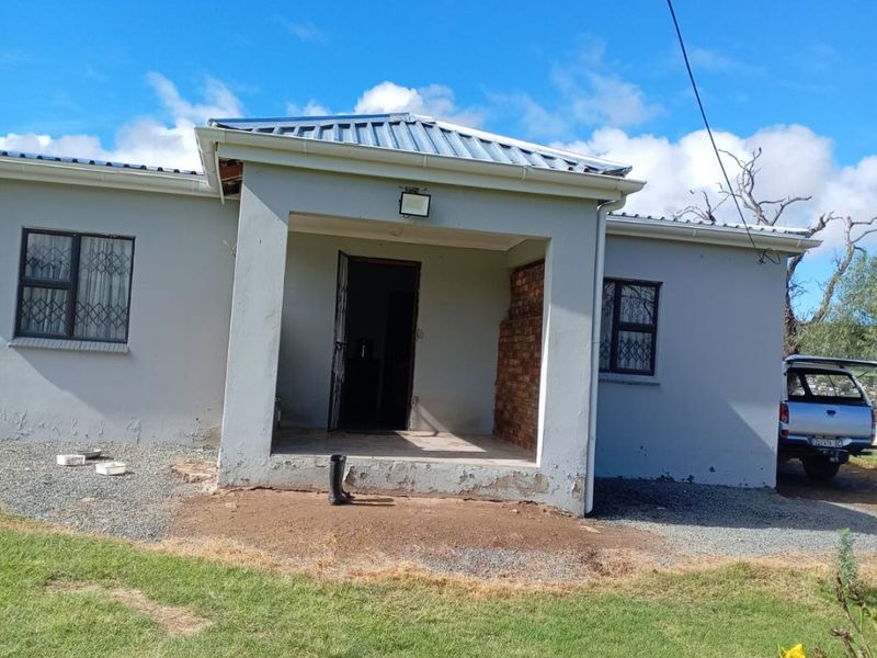 Front elevation of a farm house featuring a covered entrance porch, corrugated metal roofing, and security window bars, requiring exterior maintenance and finishing.
