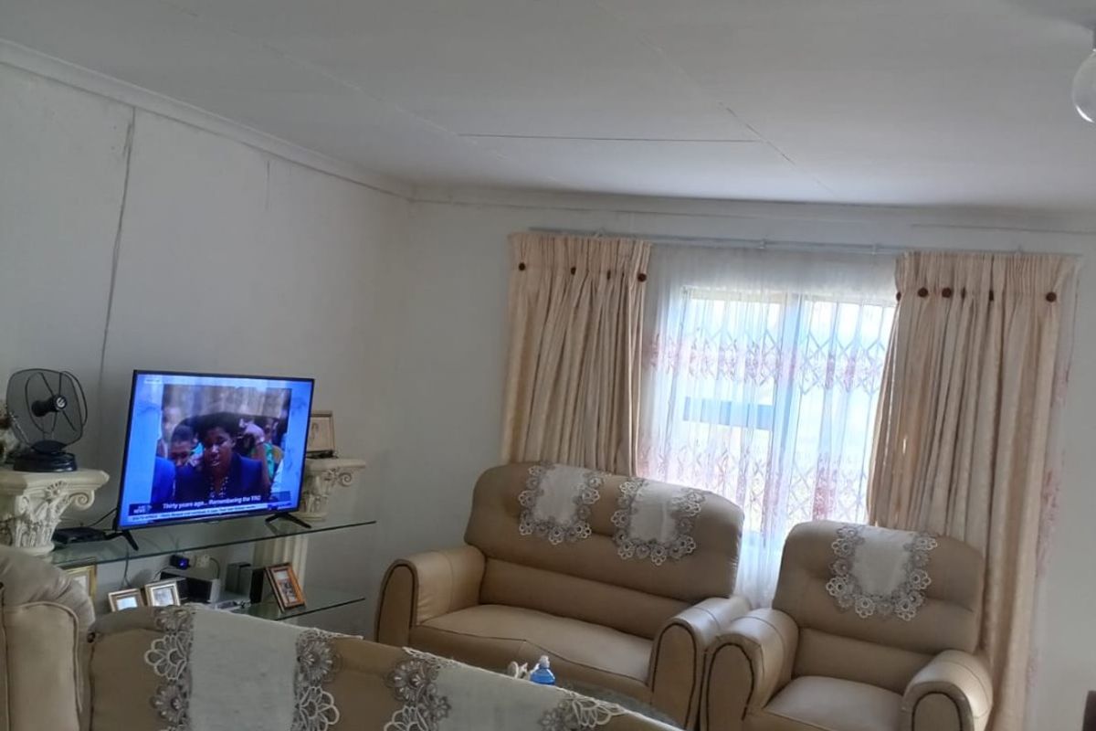 A living room area featuring tiled flooring and standard window treatments, showing signs of wear on the ceiling and wall finishes.