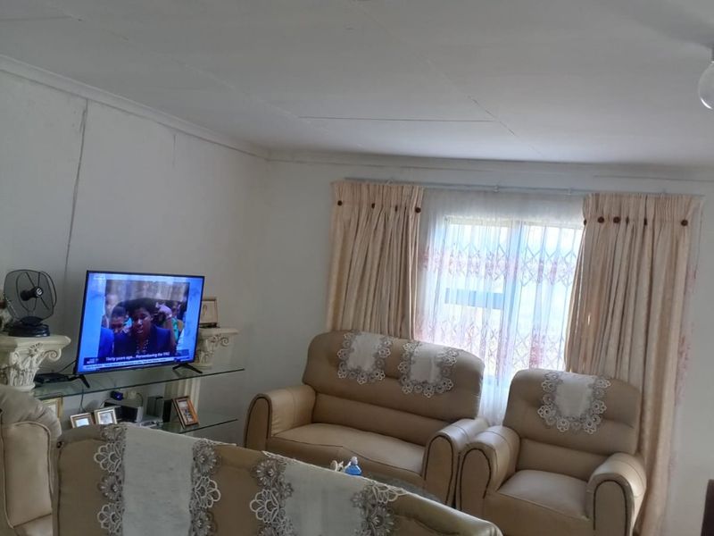 A living room area featuring tiled flooring and standard window treatments, showing signs of wear on the ceiling and wall finishes.