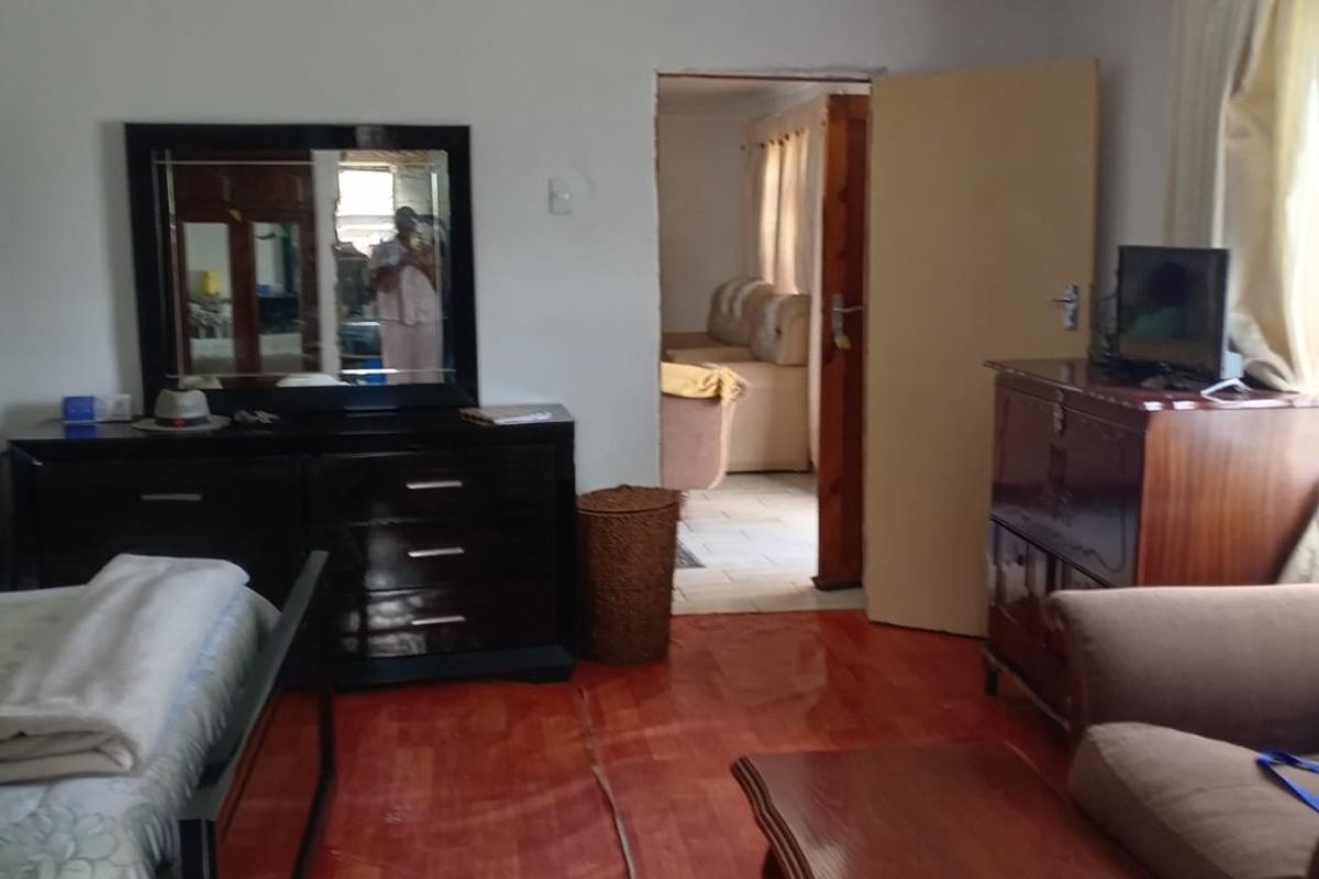 A bedroom featuring laminate flooring with a visible seam defect and basic lighting, leading into an adjacent living space.