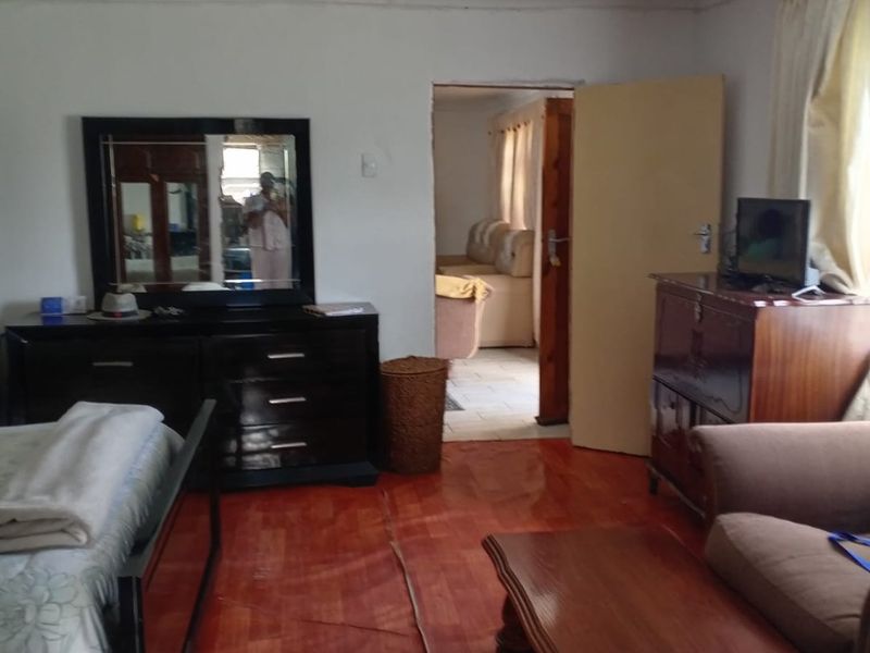 A bedroom featuring laminate flooring with a visible seam defect and basic lighting, leading into an adjacent living space.