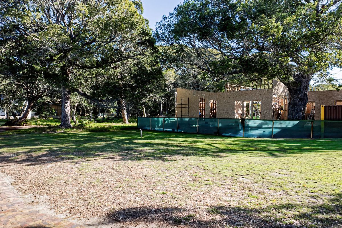 A view of a residential property under construction, featuring timber framing and mature trees on a landscaped plot.