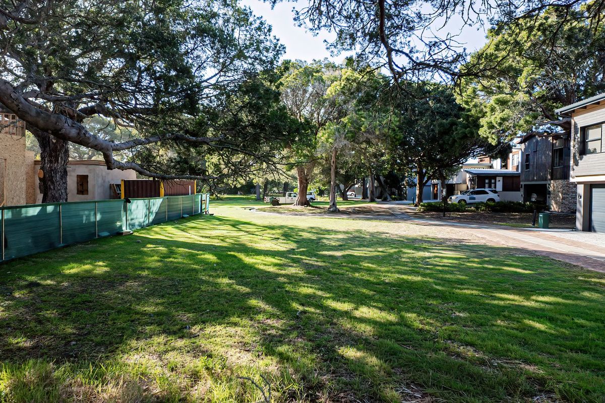 A view of a residential plot featuring mature trees, a manicured lawn, and adjacent construction activity.
