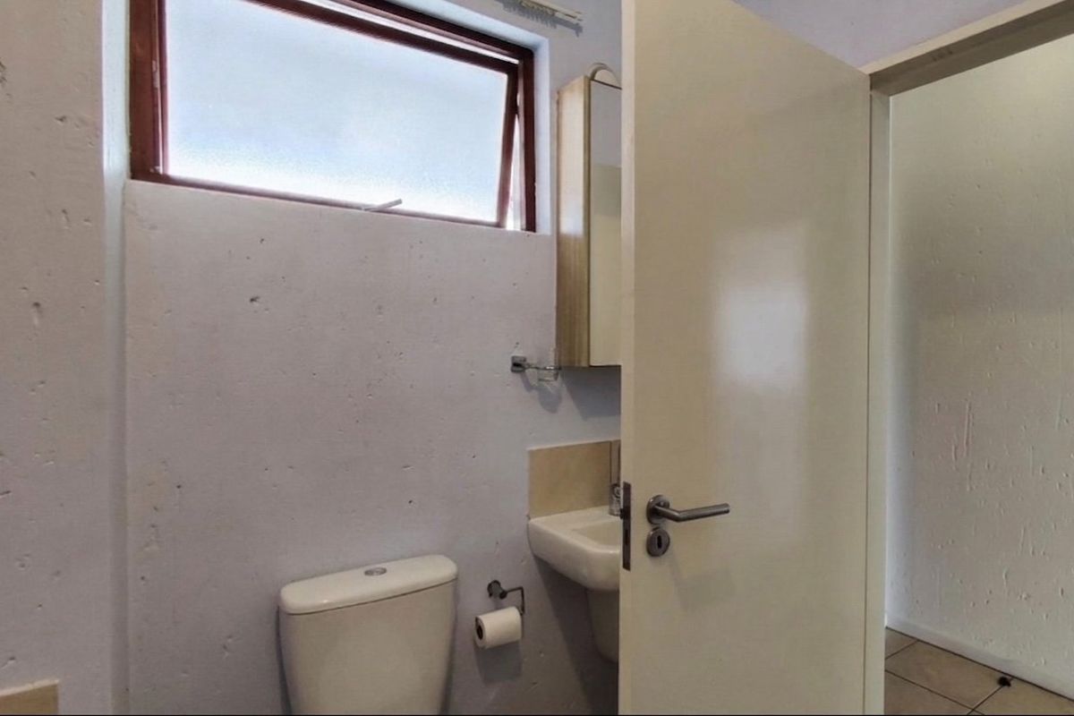 A compact bathroom featuring a wall-mounted basin, medicine cabinet, and toilet, with a top-hung window providing natural light.