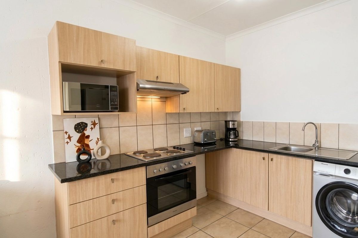 A functional kitchen featuring light wood-finish cabinetry, granite countertops, a built-in oven with hob, and tiled flooring with a dedicated space for a washing machine.