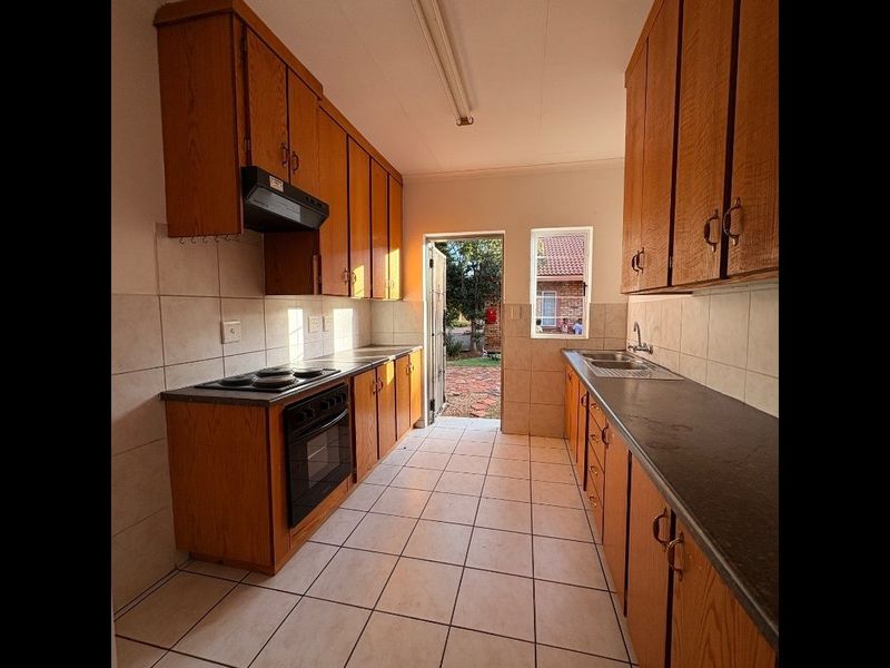 A functional galley-style kitchen featuring wooden cabinetry, built-in oven, electric hob, and direct access to the rear exterior area.