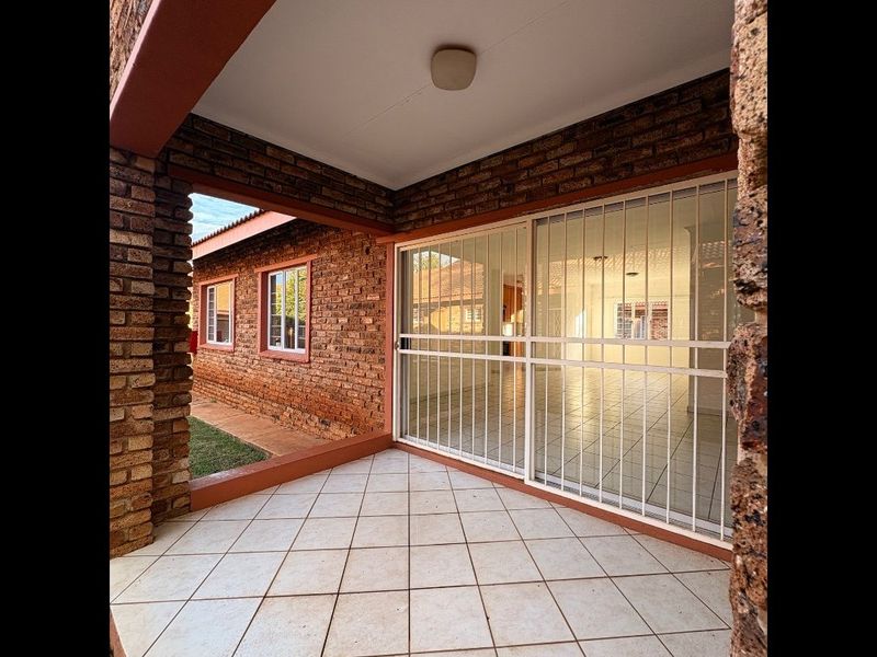 A covered patio area featuring exposed brick walls and tiled flooring, providing access to the interior living space through a secure sliding glass door.