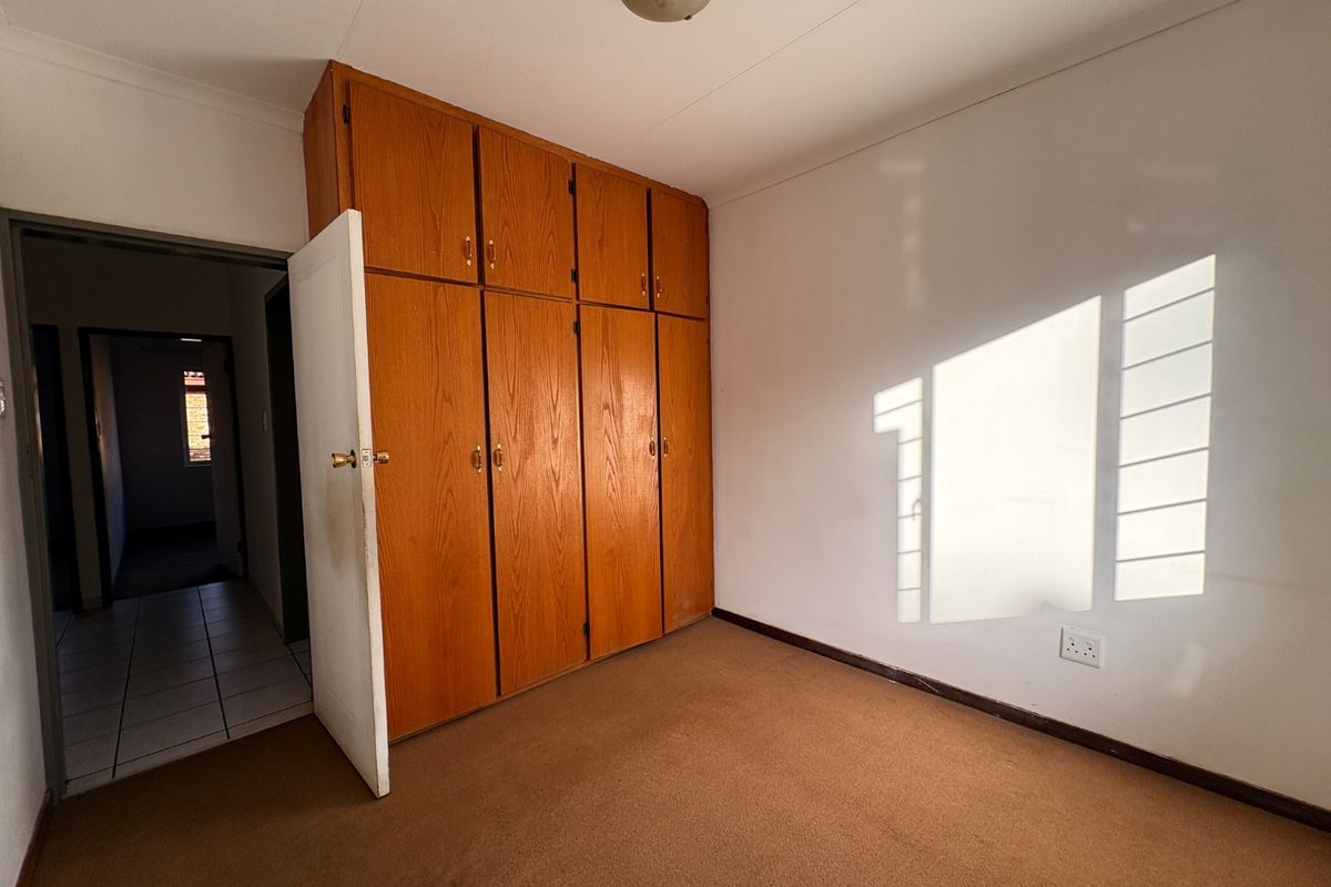 An empty bedroom featuring built-in wooden cupboards, carpeted flooring, and a ceiling light fixture, offering a blank canvas for potential updates.