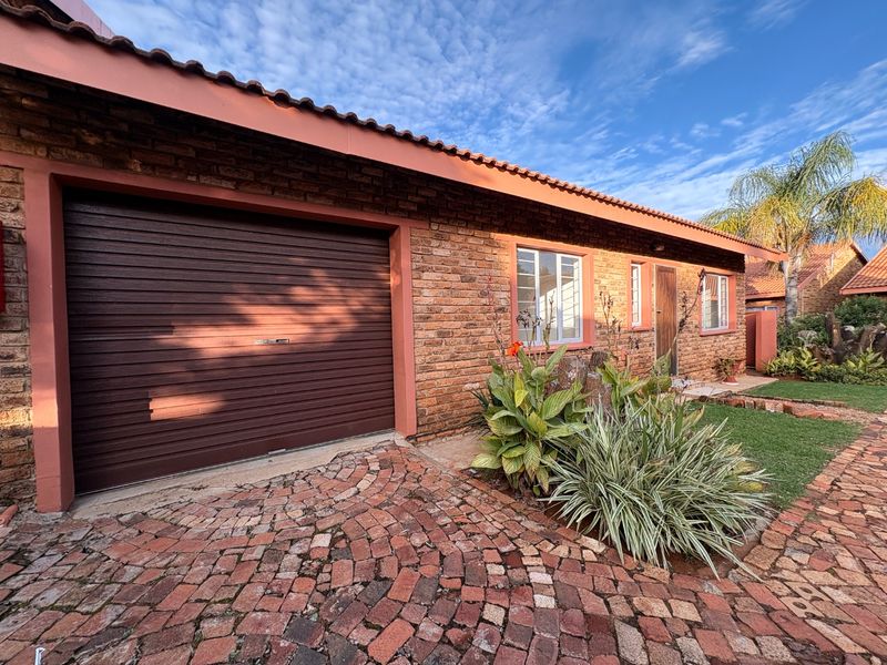 Front elevation of a townhouse featuring a face-brick facade, tiled roof, integrated roller garage door, and a decorative paved driveway.