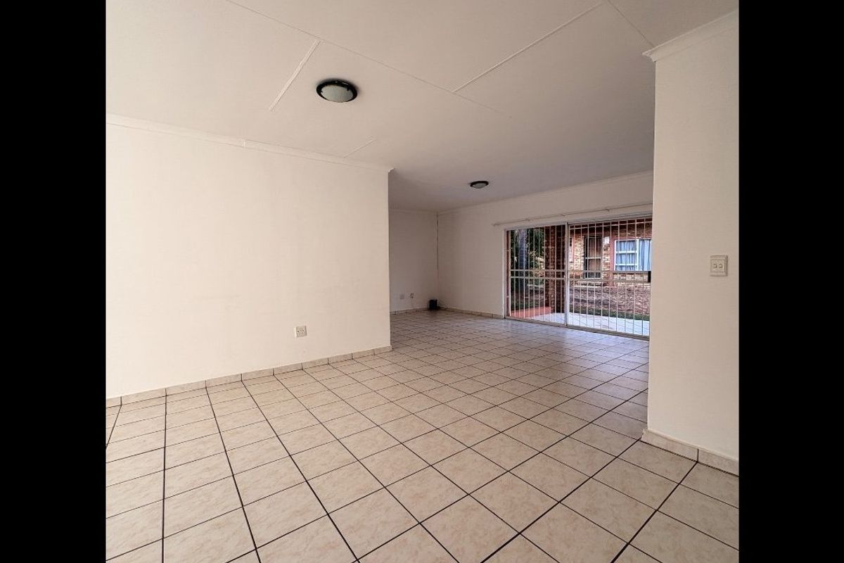 Spacious, empty living area featuring neutral tiled flooring and a sliding glass door with security gate leading to the exterior.
