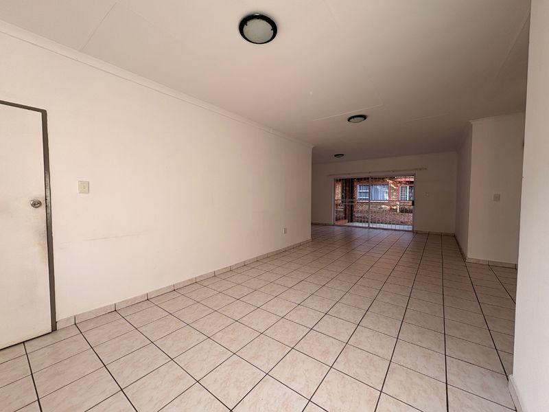 A spacious, empty open-plan living area featuring neutral ceramic floor tiles, flush mount lighting, and a sliding glass door leading to the exterior.