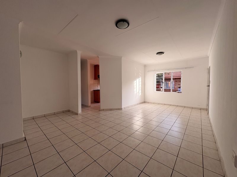 Spacious open-plan living area featuring neutral ceramic floor tiles, ample natural light, and a view into the adjacent kitchen space.