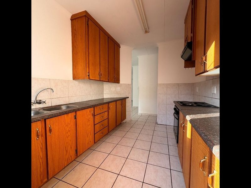 A functional kitchen featuring wooden cabinetry, laminate countertops, tiled backsplash, and built-in cooking appliances, offering a clean and practical layout.