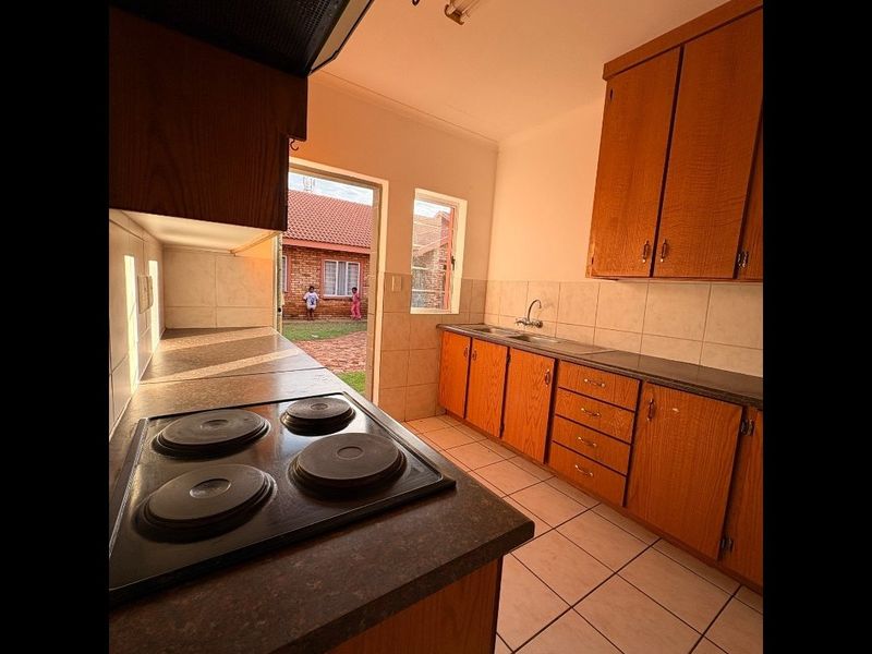 A functional kitchen featuring wooden cabinetry, an electric hob with extractor, and tiled flooring, with direct access to the rear exterior area.
