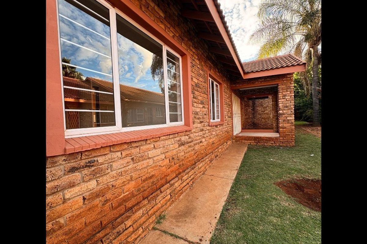 Rear view of the townhouse featuring a face brick facade, tiled roof, security bars on windows, and a small covered patio area.