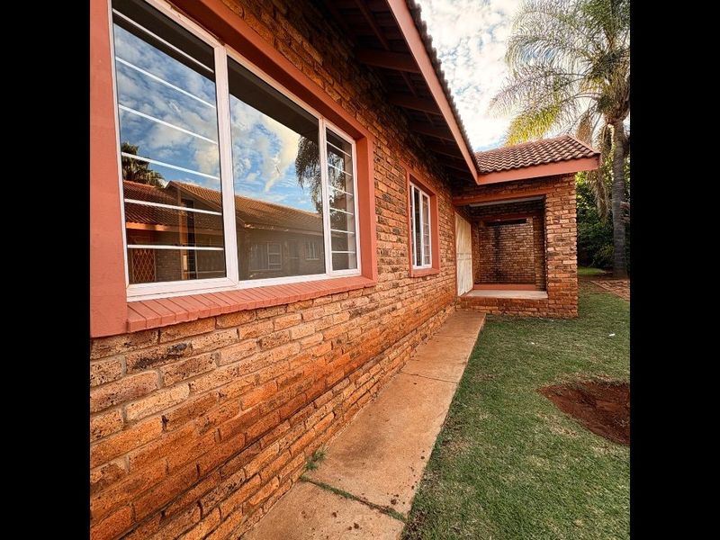 Rear view of the townhouse featuring a face brick facade, tiled roof, security bars on windows, and a small covered patio area.