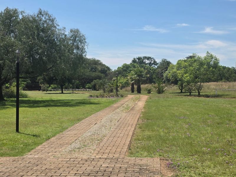 A spacious, well-maintained farm garden featuring a paved driveway, mature trees, and open green lawns.