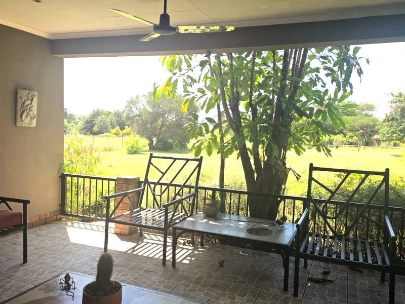 A covered patio featuring tiled flooring, a ceiling fan, and metal railings, offering an open view of the surrounding farm landscape.