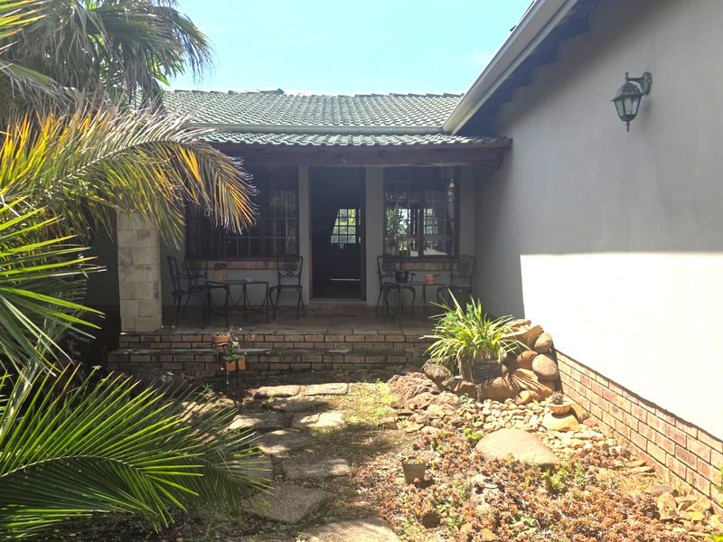 A covered patio area featuring brick foundations and stone paving, leading to a garden space with established landscaping.