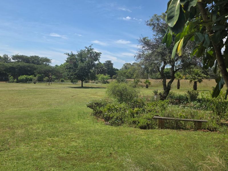 A spacious, well-maintained farm garden featuring expansive green lawns, mature trees, and established garden beds.
