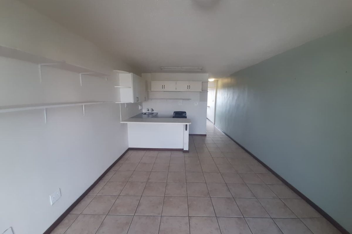 An empty open-plan living and kitchen area featuring tiled flooring, built-in cabinetry, and wall-mounted shelving, offering a blank canvas for renovation.