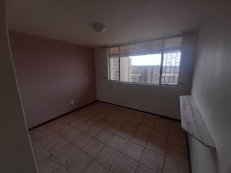 An empty bedroom featuring tiled flooring, a wall-mounted shelf, and metal security bars on the window with views of surrounding buildings.