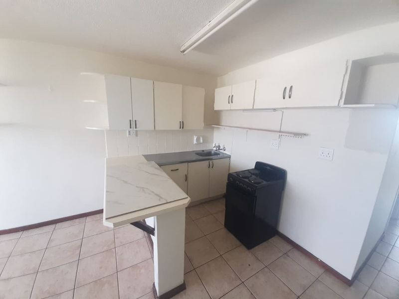 A functional kitchen featuring white cabinetry, a breakfast bar, tiled flooring, and a freestanding stove, offering a blank canvas for renovation.