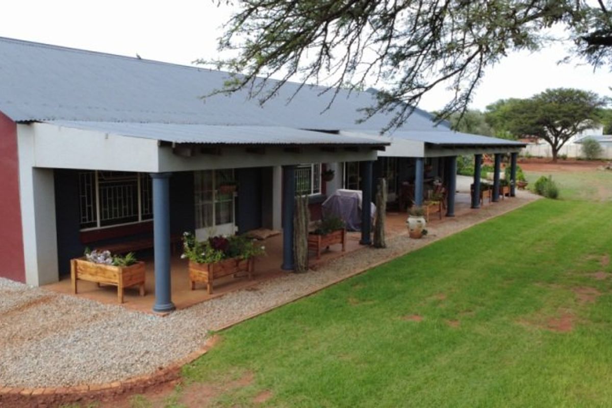 A spacious rear exterior view of the farmhouse featuring a long covered patio, corrugated metal roofing, and expansive surrounding garden grounds.