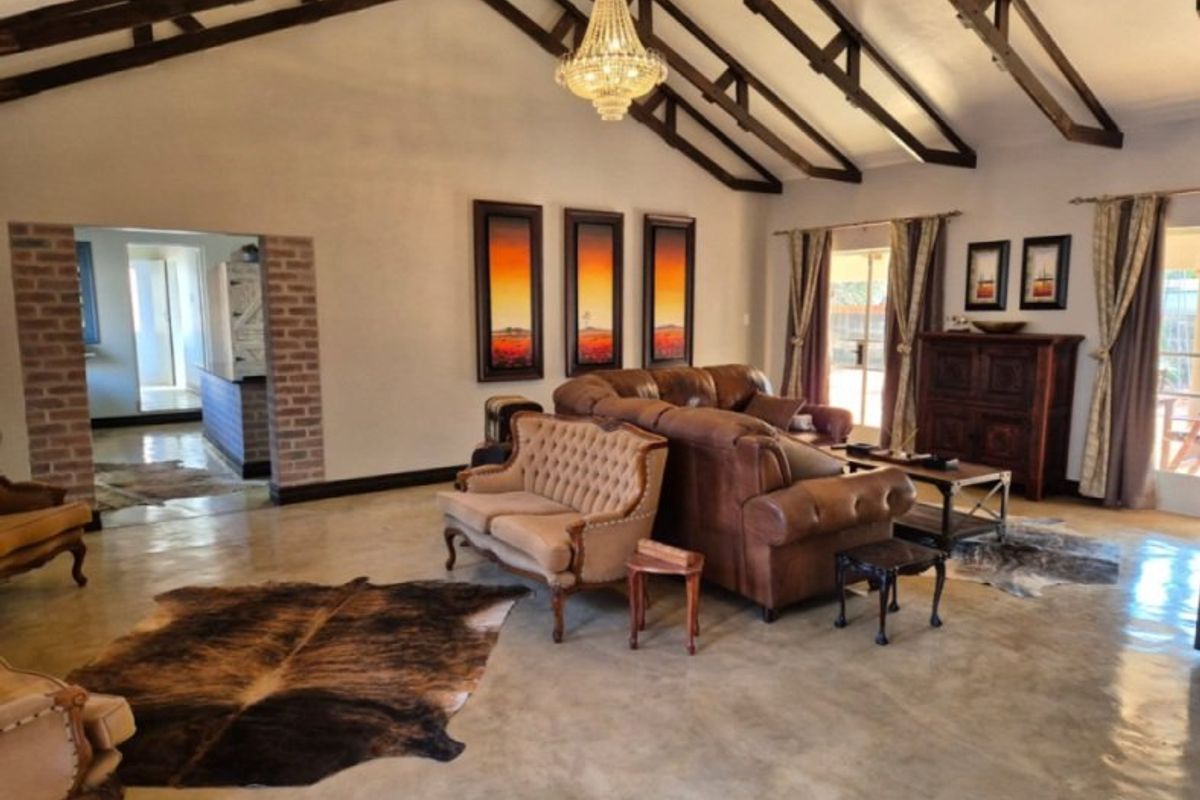Spacious living area featuring high vaulted ceilings with exposed timber trusses, polished concrete floors, and an exposed brick transition to the adjacent space.