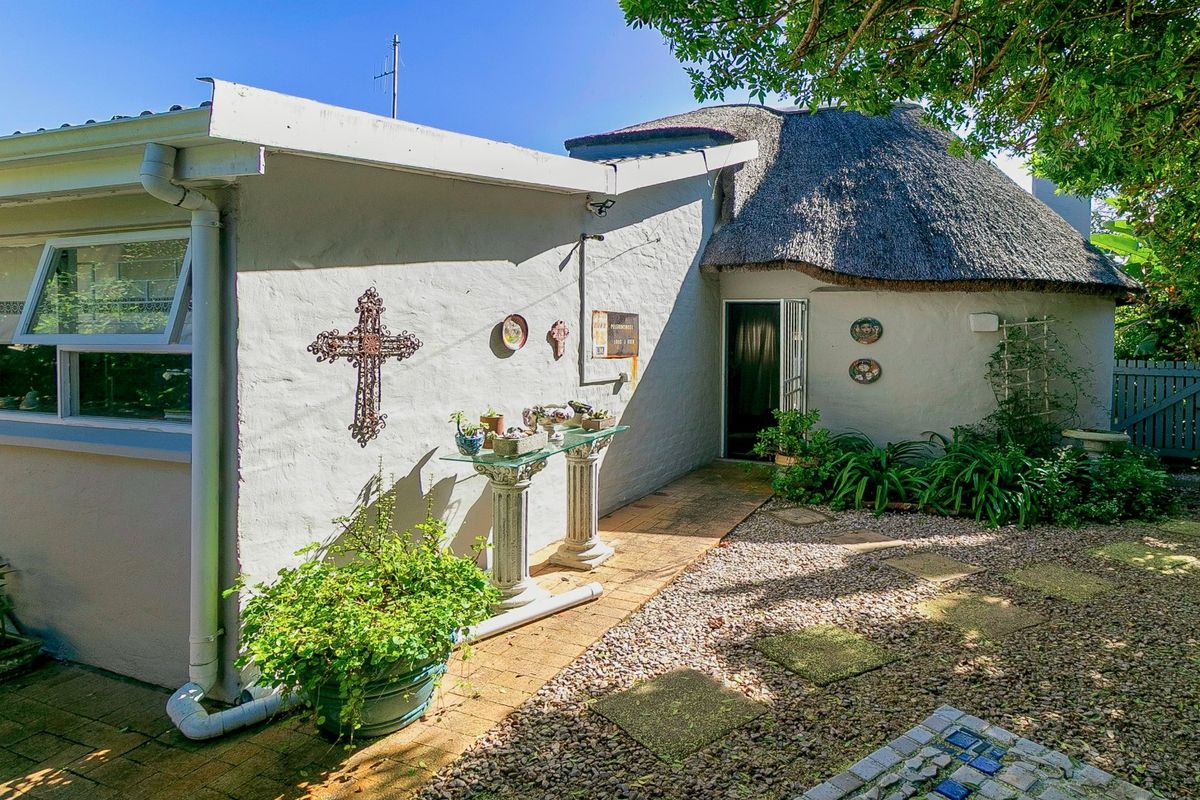 Rear exterior view of the property featuring a traditional thatched roof section, paved walkway, and gravel garden area.