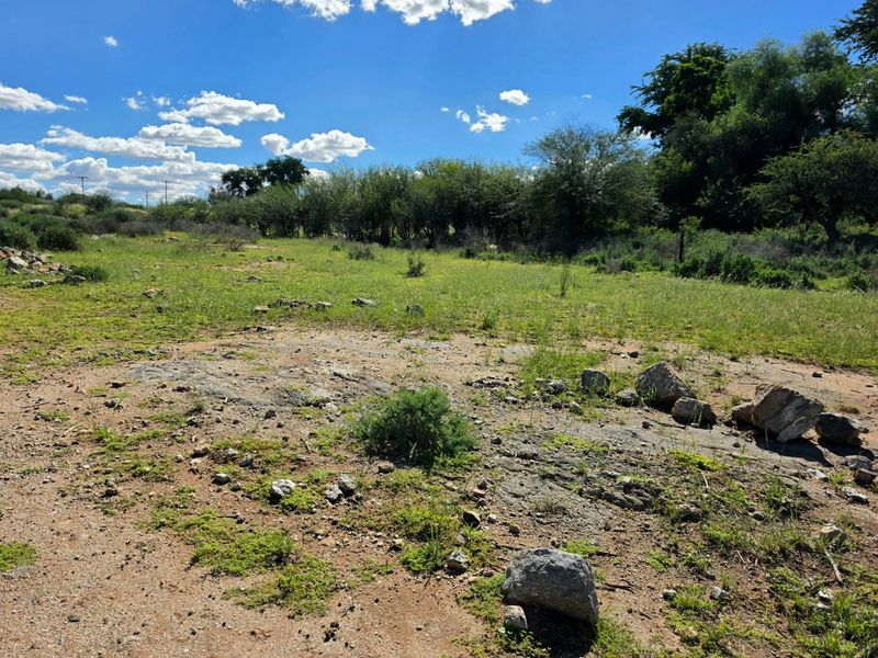 A view of the vacant residential land featuring natural vegetation and rocky terrain under a clear blue sky.