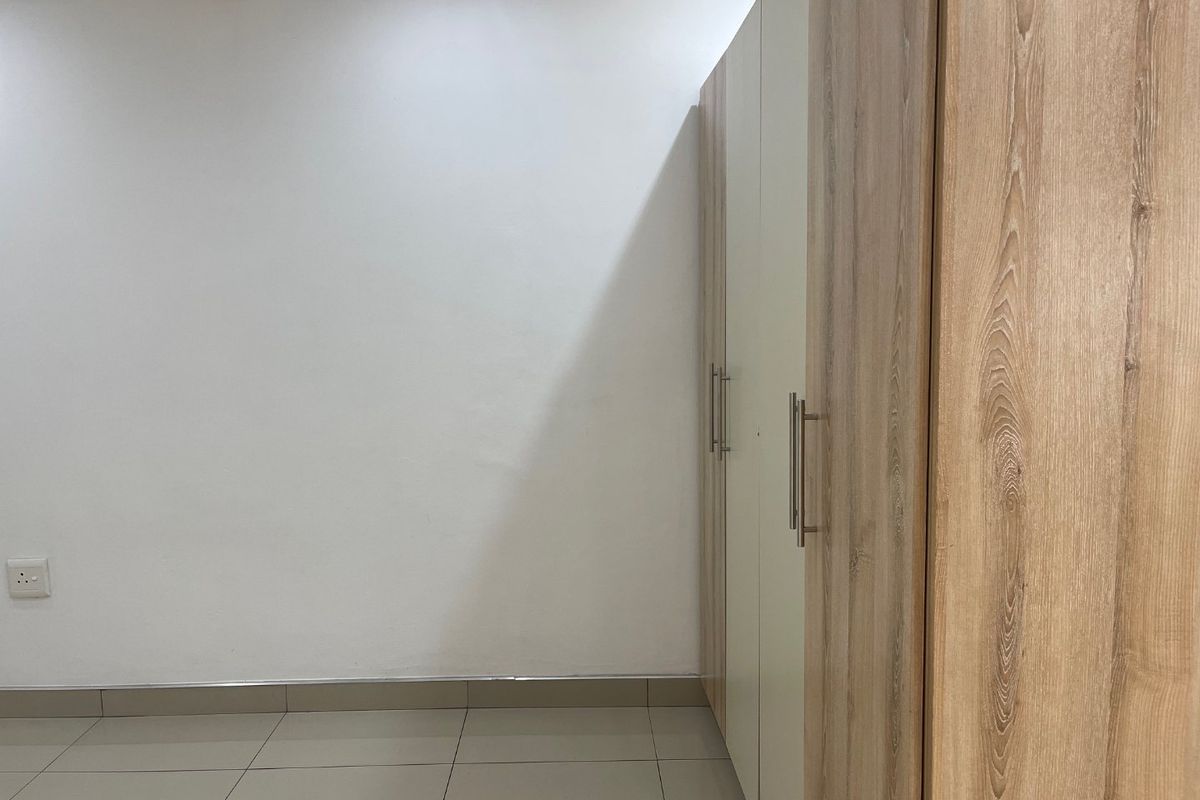 A clean, minimalist bedroom space featuring neutral tiled flooring and modern, light wood-finish built-in cupboards.