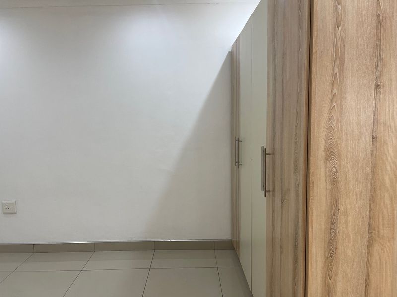 A clean, minimalist bedroom space featuring neutral tiled flooring and modern, light wood-finish built-in cupboards.