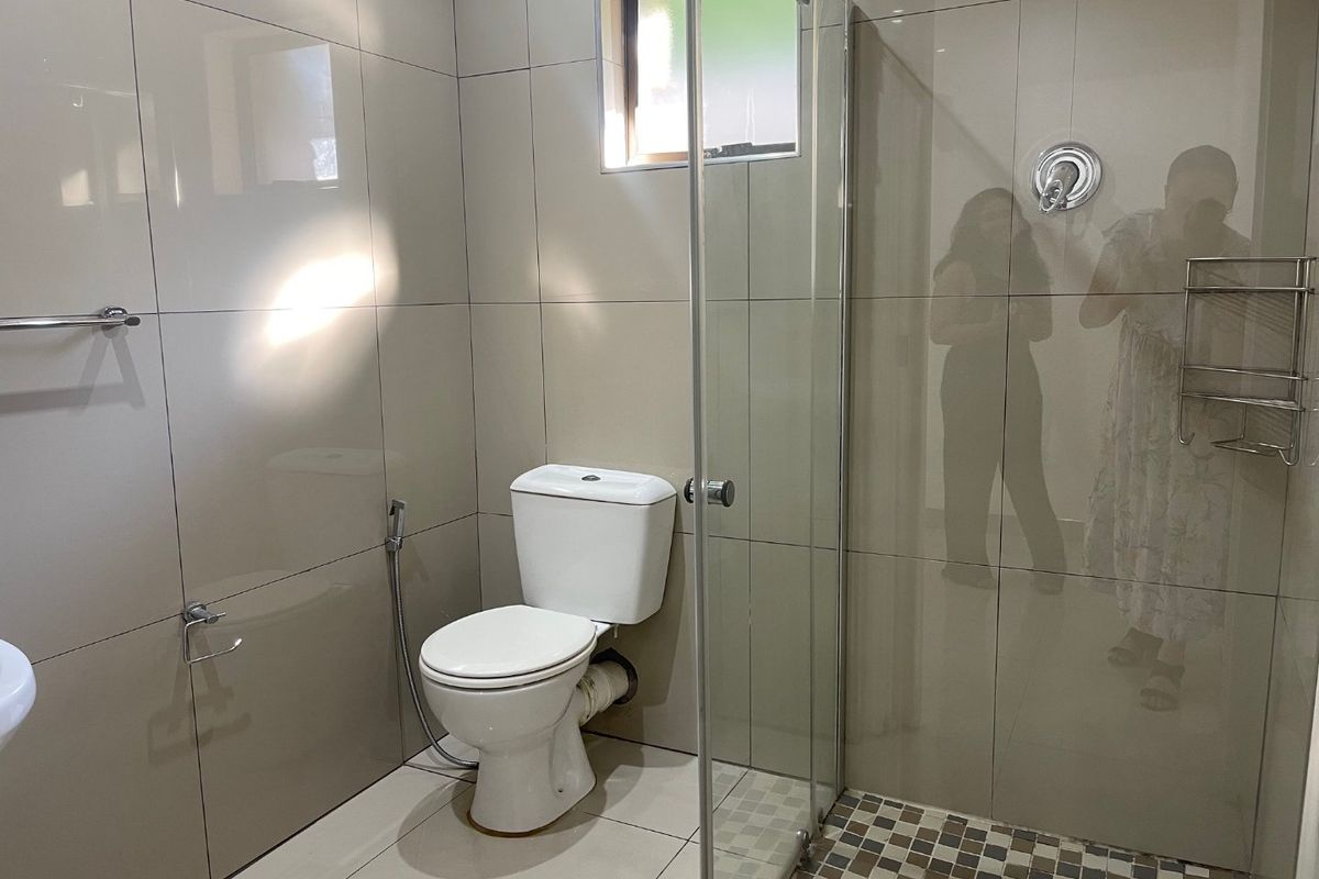 A modern bathroom featuring full-height wall tiling, a glass-enclosed shower, and a standard toilet with a bidet spray attachment.