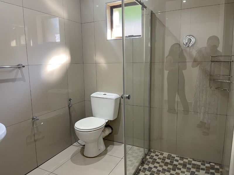 A modern bathroom featuring full-height wall tiling, a glass-enclosed shower, and a standard toilet with a bidet spray attachment.