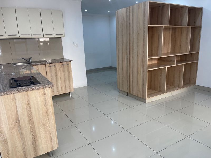 Modern kitchen featuring light wood-finish cabinetry, granite countertops, integrated hob, and a large built-in shelving unit, set against neutral tiled flooring.