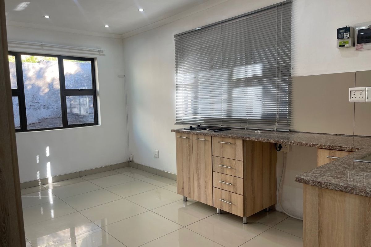 A clean, modern kitchen featuring light wood cabinetry, granite countertops, a built-in hob, and neutral tiled flooring, offering a functional and bright workspace.
