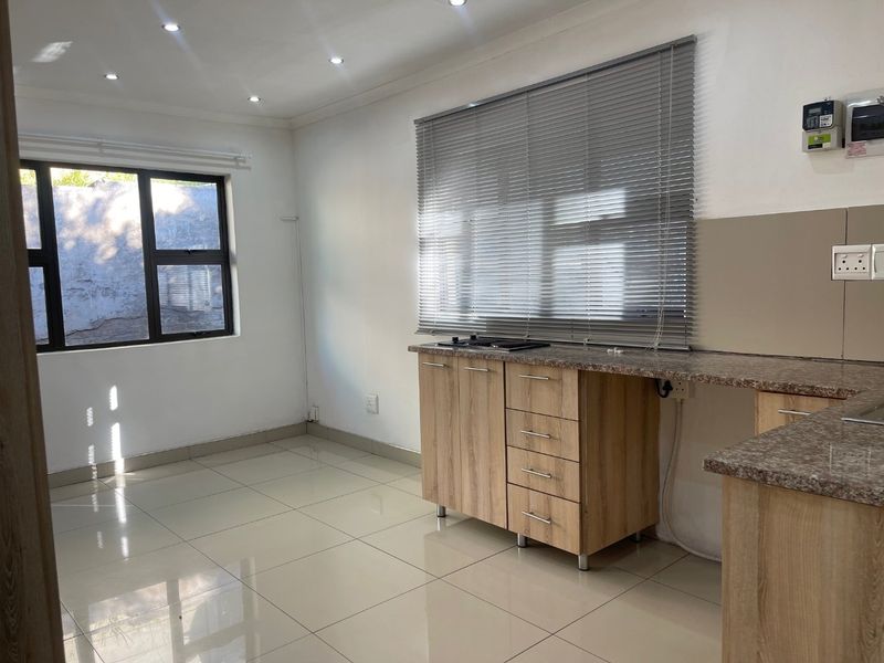 A clean, modern kitchen featuring light wood cabinetry, granite countertops, a built-in hob, and neutral tiled flooring, offering a functional and bright workspace.
