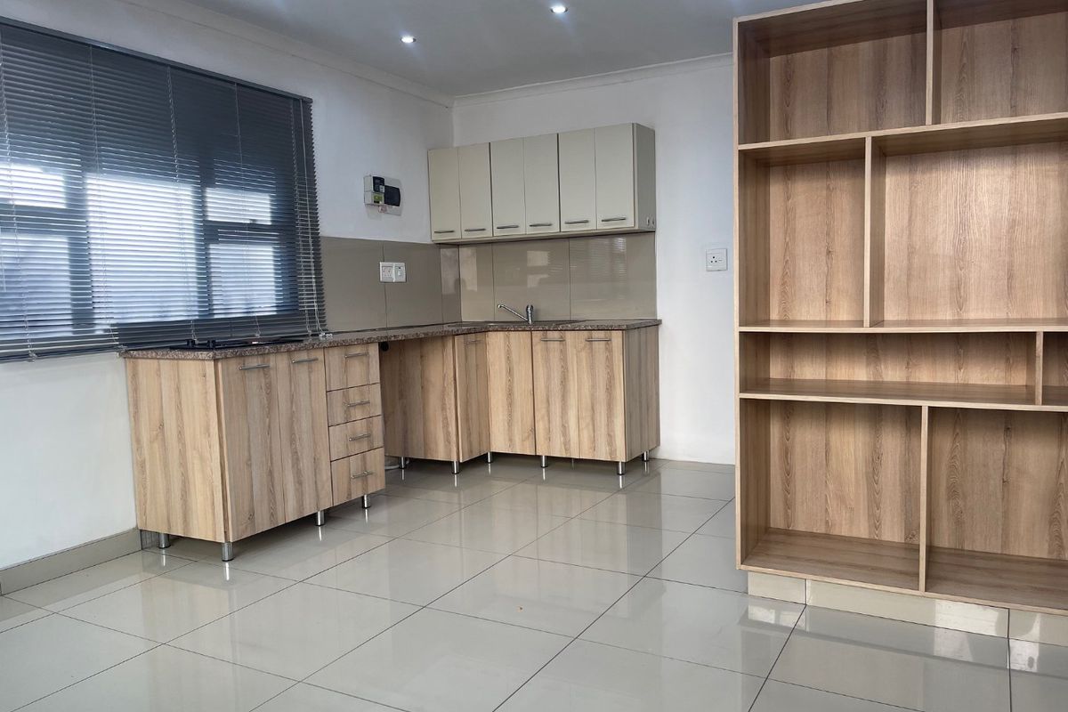 A clean, modern kitchen featuring light wood-finish cabinetry, granite countertops, a built-in hob, and neutral tiled flooring in an open-plan layout.