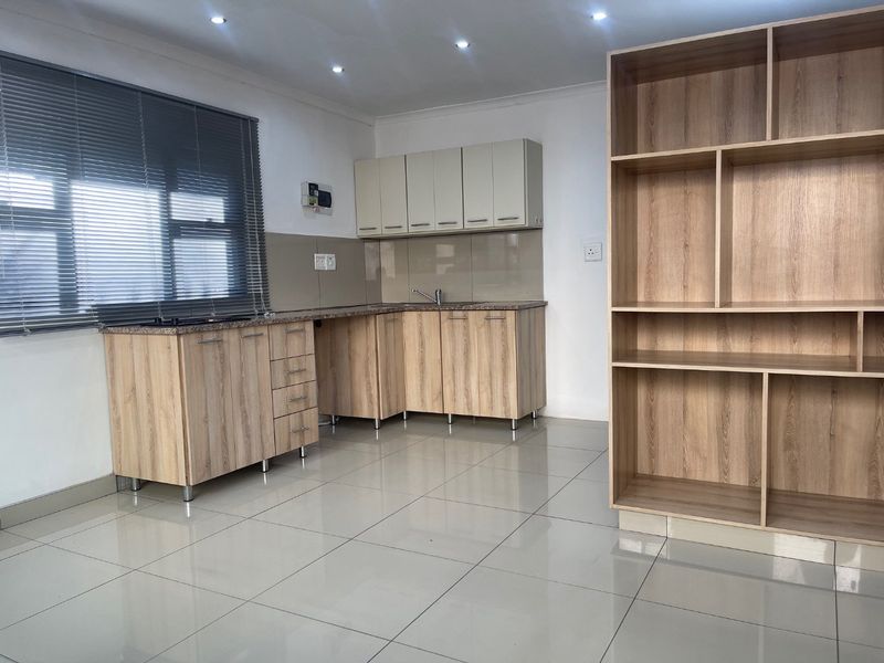 A clean, modern kitchen featuring light wood-finish cabinetry, granite countertops, a built-in hob, and neutral tiled flooring in an open-plan layout.